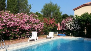 Piscina com cadeiras de espreguiçadeira brancas e um guarda-sol listrado em vermelho e branco.