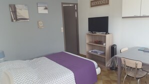 Une chambre à coucher comprenant un lit, un bureau, une chaise, un téléviseur et une étagère avec des livres et un objet décoratif.