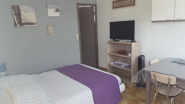 Un dormitorio con cama, escritorio, silla, televisor y estante con libros y un adorno.