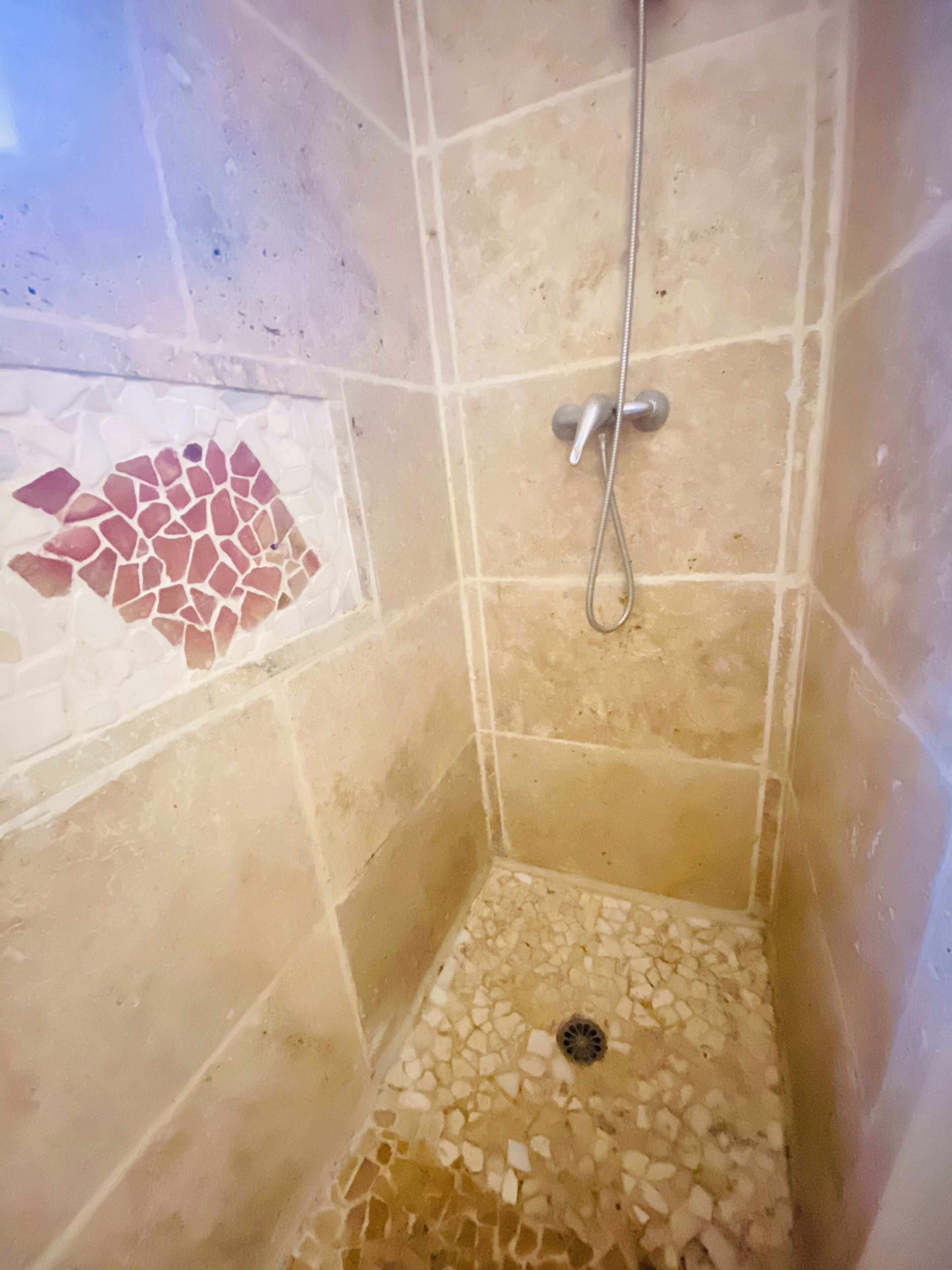 A small shower area with tiled walls and floor, a showerhead, and a drain.