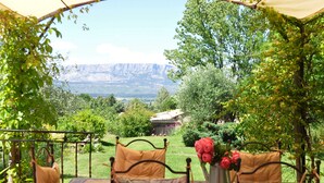 An outdoor seating area with a view of mountains, surrounded by greenery and a small building. - Exceptional - Property with full view of Mont Ste Victoire (Trets)