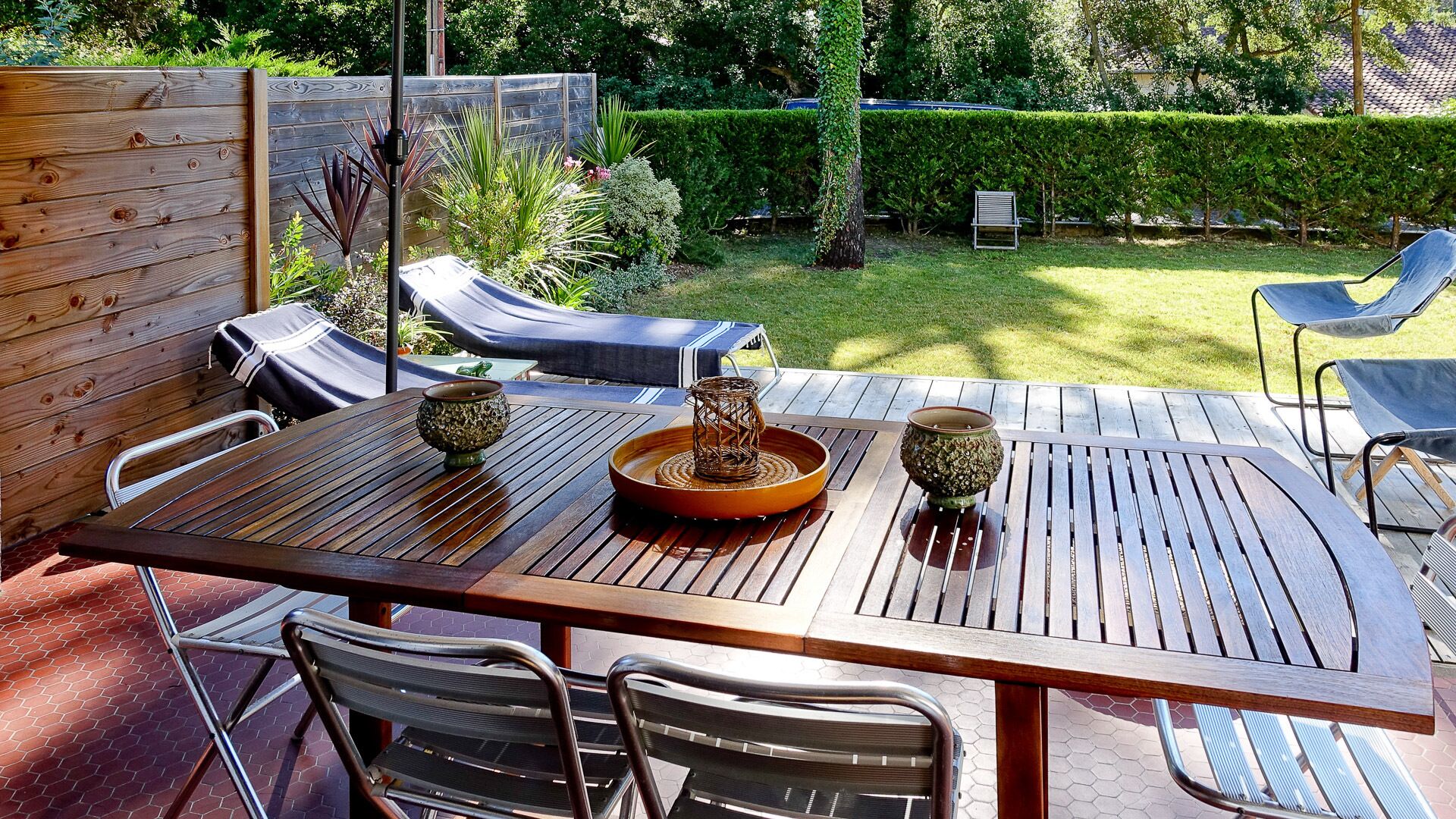 Eine Terrasse im Freien mit einem Holztisch, Metallstühlen und einem gepolsterten Loungesessel.