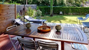Eine Terrasse im Freien mit einem Holztisch, Metallstühlen und einem gepolsterten Loungesessel.