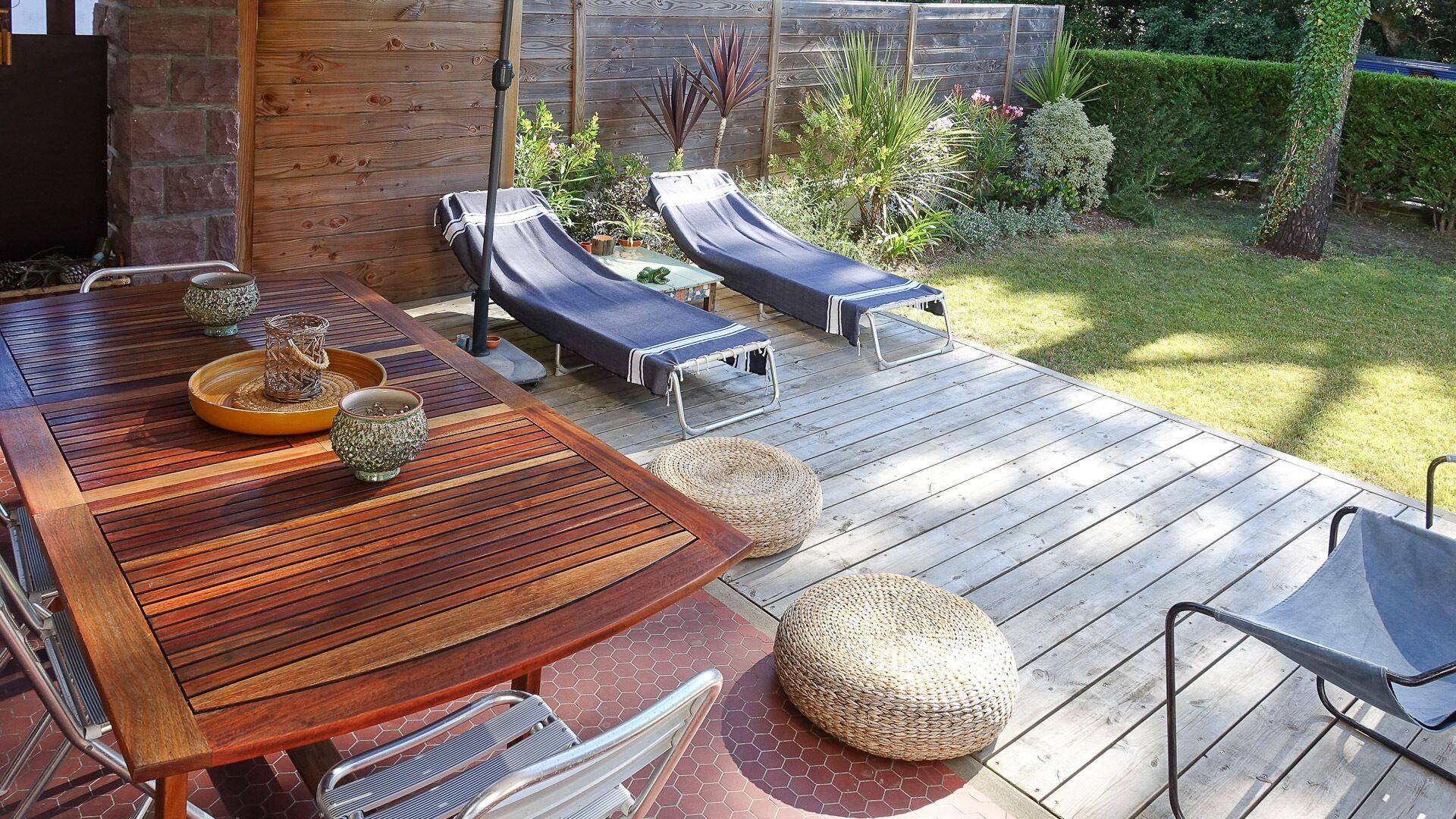 A wooden deck with a dining table, lounge chairs, and woven poufs.