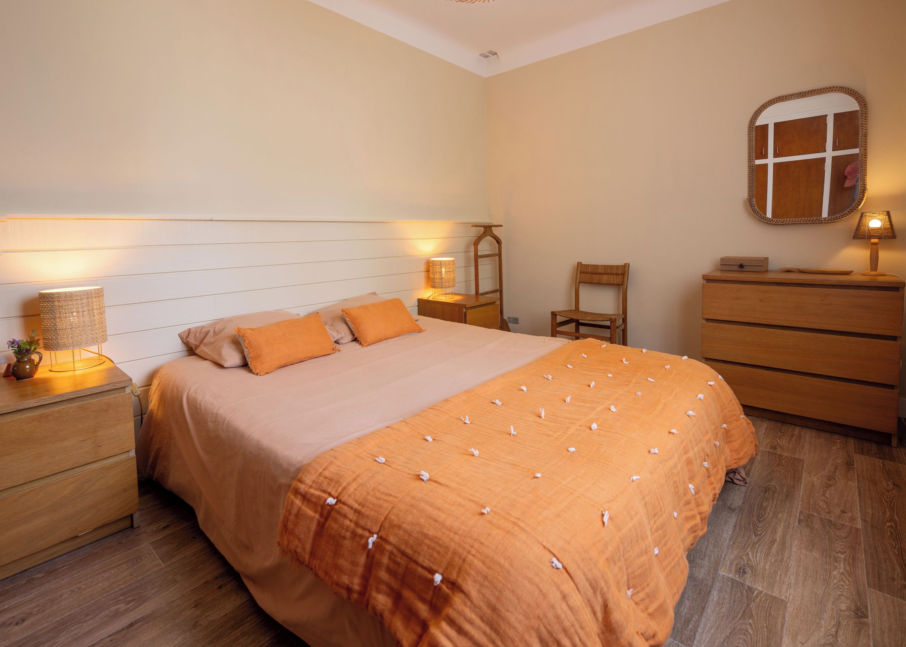 A neatly arranged bedroom with a large bed, bedside tables with lamps, a wooden dresser, and a mirror on the wall.