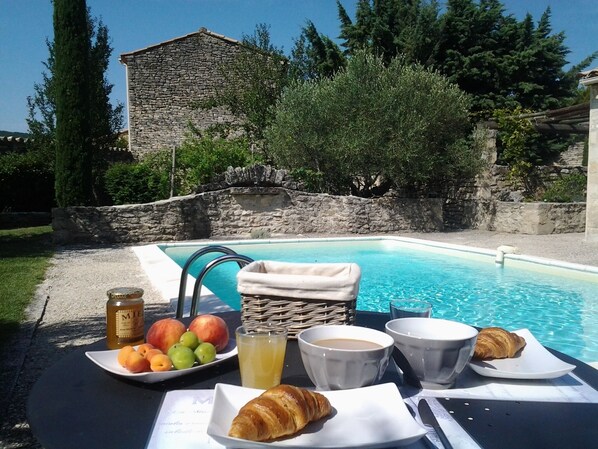 A poolside breakfast setup with fruits, croissants, and beverages, surrounded by stone walls and greenery. - Charming cottage Gordes, private pool, very quiet, views, New 2025: Optics fiber (Gordes)