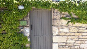 Un mur de pierre avec une porte en bois, envahi par du lierre vert, et une petite enseigne au-dessus de la porte.