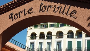 Une arche surmontée de l’inscription « Gorge Forville », au-dessus d’un immeuble doté de nombreux balcons et fenêtres.