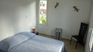 A bedroom with a bed, a chair, a nightstand, a lamp, and a window.