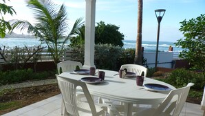 An outdoor dining area with a white table and chairs, set against a backdrop of a coastal view.