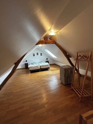 Une chambre située dans un espace de type « loft », avec un plancher en bois, un lit, une petite table et un portant à vêtements suspendu.