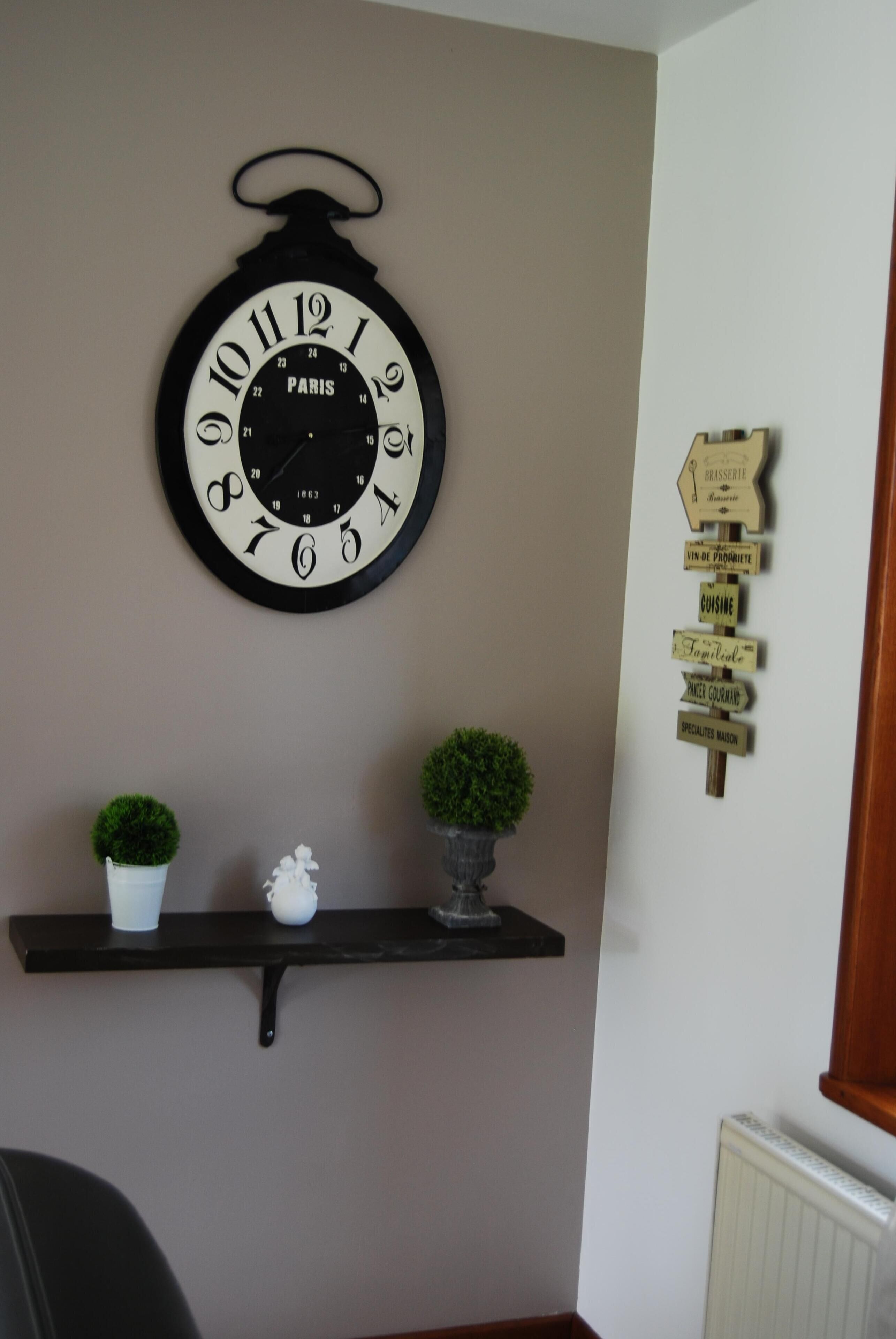 Une horloge murale au design parisien, un panneau de signalisation et deux plantes en pot placés sur une étagère.