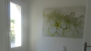 Un dormitorio con cama, ventana, mesita de noche con lámpara y decoración floral en la pared.