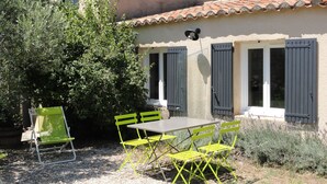 Un patio con una mesa y sillas, una silla plegable verde y una casa con techo de tejas y contraventanas.