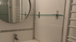 Un baño con un lavamanos blanco, un espejo redondo y un estante de vidrio.