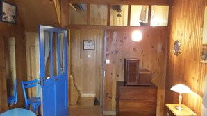 A wooden room with a blue door, a small table with a lamp, a chair, and a cabinet.