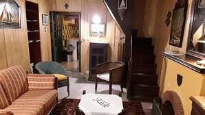 A cozy living room with a sofa, a small table, and a chair. A staircase leads to another room.