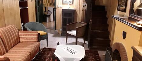 Una sala de estar acogedora con un sofá, una mesita y un sillón. Una escalera conduce a otra habitación.