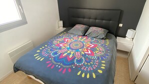 A bedroom with a bed, a black headboard, a colorful bedspread, and a window. - Loriot1 apartment sea view on the fort blocked, ploemeur  (Ploemeur)