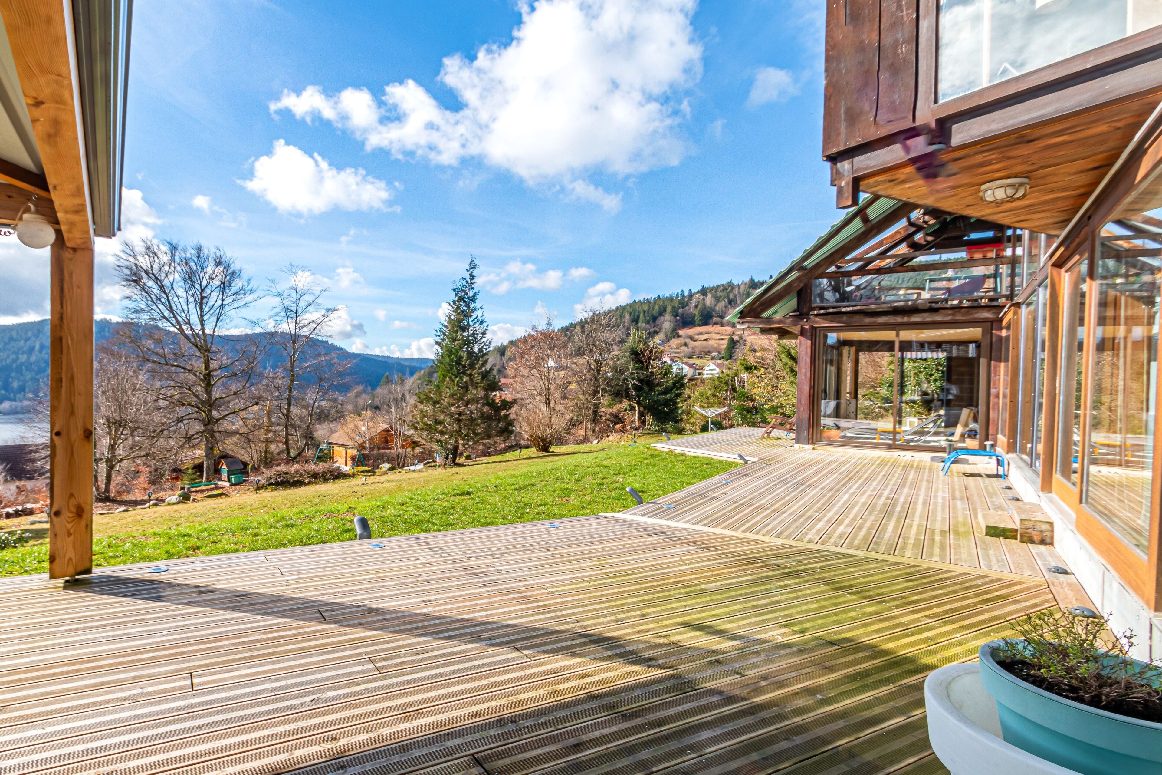 A wooden deck with a view of a mountainous landscape, a glass door entrance, and a potted plant.
