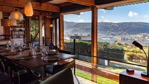 Un comedor con una mesa dispuesta para comer, grandes ventanales que ofrecen vistas a un paisaje montañoso.
