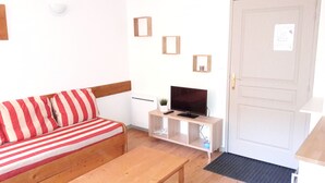 Een kleine, knusse kamer met een gestreepte bank, een televisie op een houten standaard en een deur met een berichtje.
