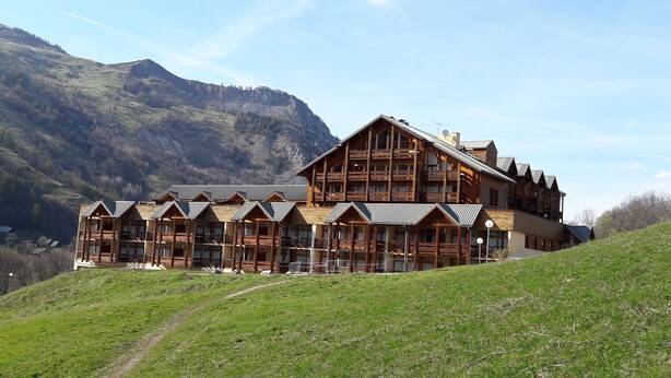 Een groot houten hotel met meerdere balkons en een berg op de achtergrond.