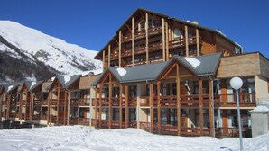 Een houten lodge met meerdere balkons en grote ramen, omringd door met sneeuw bedekte bergen.