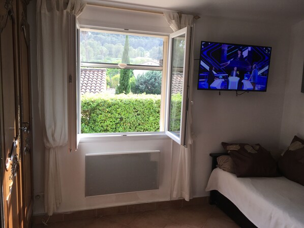 A bedroom with a large window, a radiator, a bed, and a TV mounted on the wall.