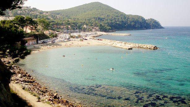 A coastal town with a beach, clear waters, and a mountainous backdrop.