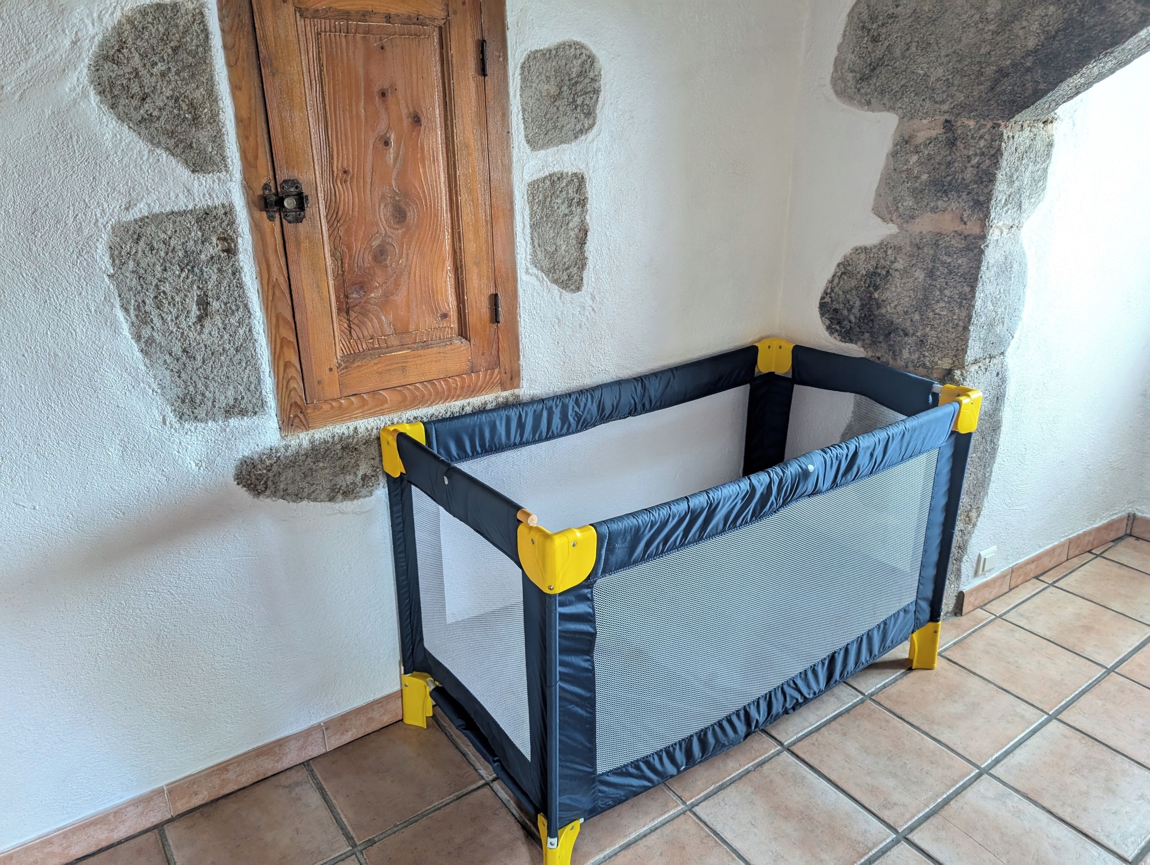 A corner room with a baby playpen against a wall with stone patches and a wooden door.