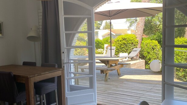 A dining area with a wooden table and chairs, a hanging light fixture, and a view of an outdoor patio with a table and chairs. - Lake view, Exceptional location between Lake and Ocean, all within walking distance (Soorts-Hossegor)