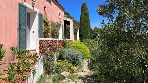 A building with a pink facade, green shutters, and a stone pathway leading to a covered area.