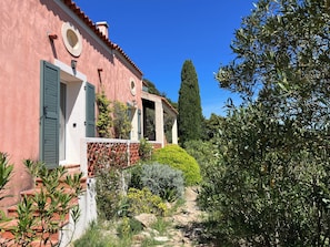 Un bâtiment à la façade rose, aux volets verts et à l’allée pavée qui mène à un espace abrité.