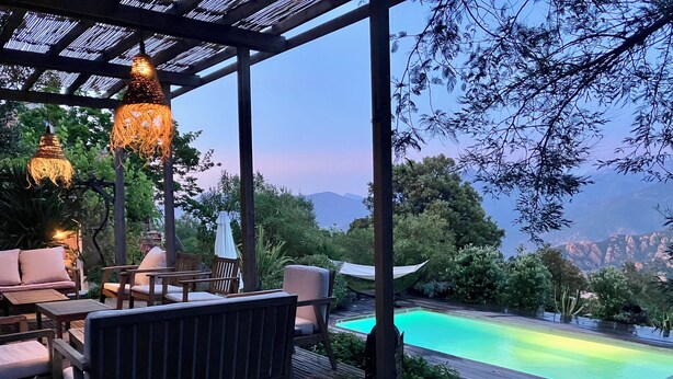 A covered outdoor area with seating, a pool, and a view of mountains.