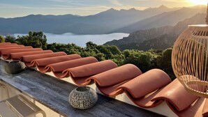 A terrace with lounge chairs, a decorative vase, and a view of mountains and a lake.