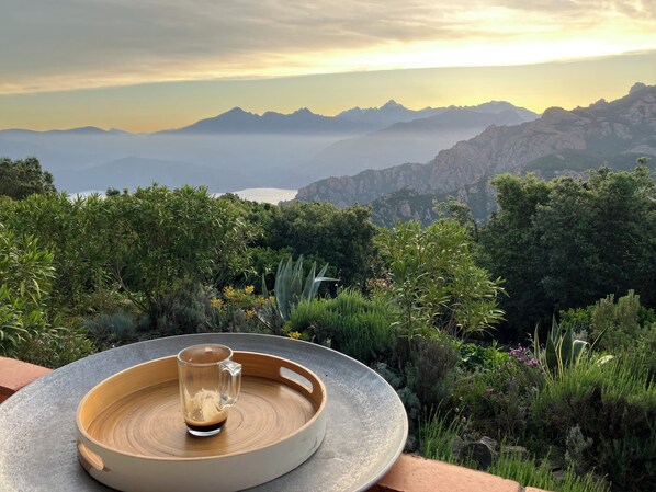 A table with a glass and a cup, surrounded by lush greenery and mountains in the background.