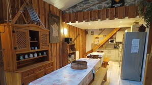 Une cuisine rustique avec des meubles de rangement en bois, une table à manger recouverte d’une nappe matelassée et un réfrigérateur.