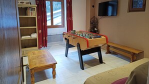 Une pièce chaleureuse avec un baby-foot, un banc en bois, une bibliothèque et un téléviseur fixé au mur.