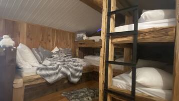 A cabin with wooden walls and a sloped ceiling. There are bunk beds with white bedding and a ladder. A fur rug is on the wooden floor.