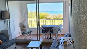 A living room with a sofa, a coffee table, and a TV. There is a balcony with a table and chairs, and a view of the sea. - cap d'agde t3 apartment 54m2 facing the sea seafront with sea views (Agde)