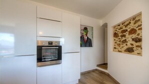 A modern kitchen with white cabinetry, a built-in oven, and a stone wall art piece.