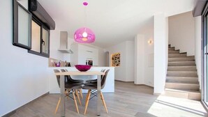 A modern kitchen with a dining table, chairs, and a pink pendant light.