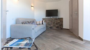 A modern living room with a sofa, a flat-screen TV mounted on a stone wall, and a magazine on a coffee table.