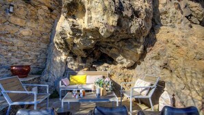 A stone wall, a wooden bench, a sofa with cushions, and two chairs in a rocky outdoor setting.