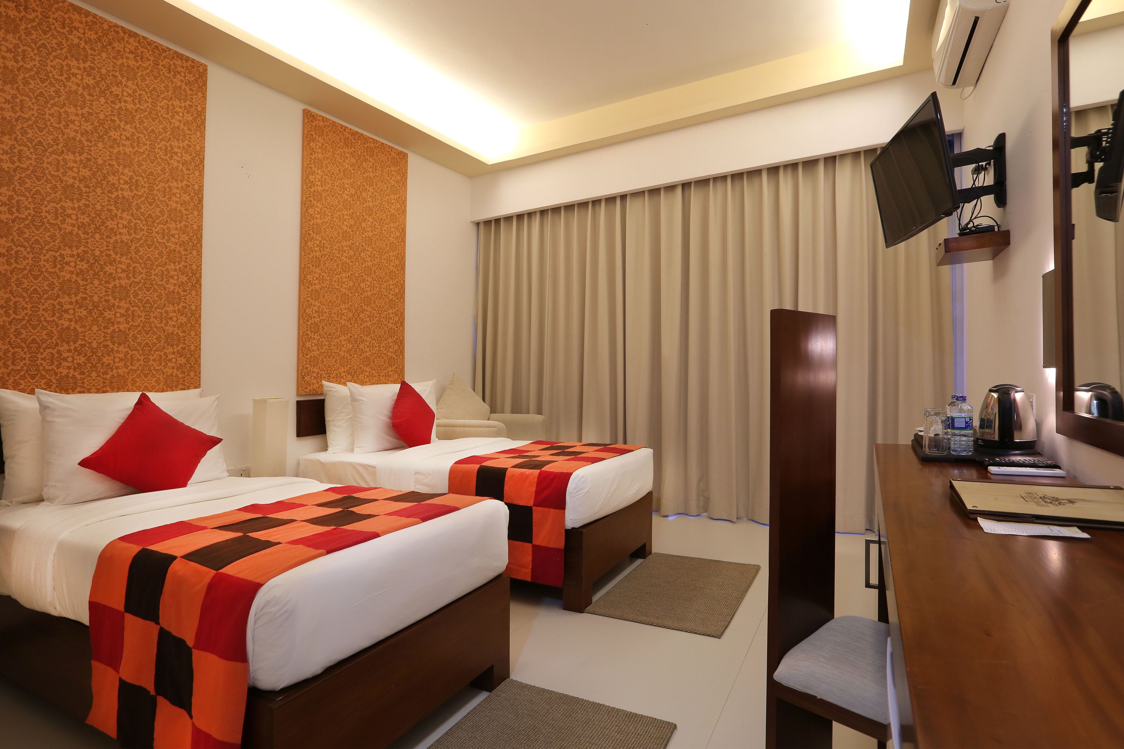 A hotel room with two beds, a desk, a TV, and a window with curtains.
