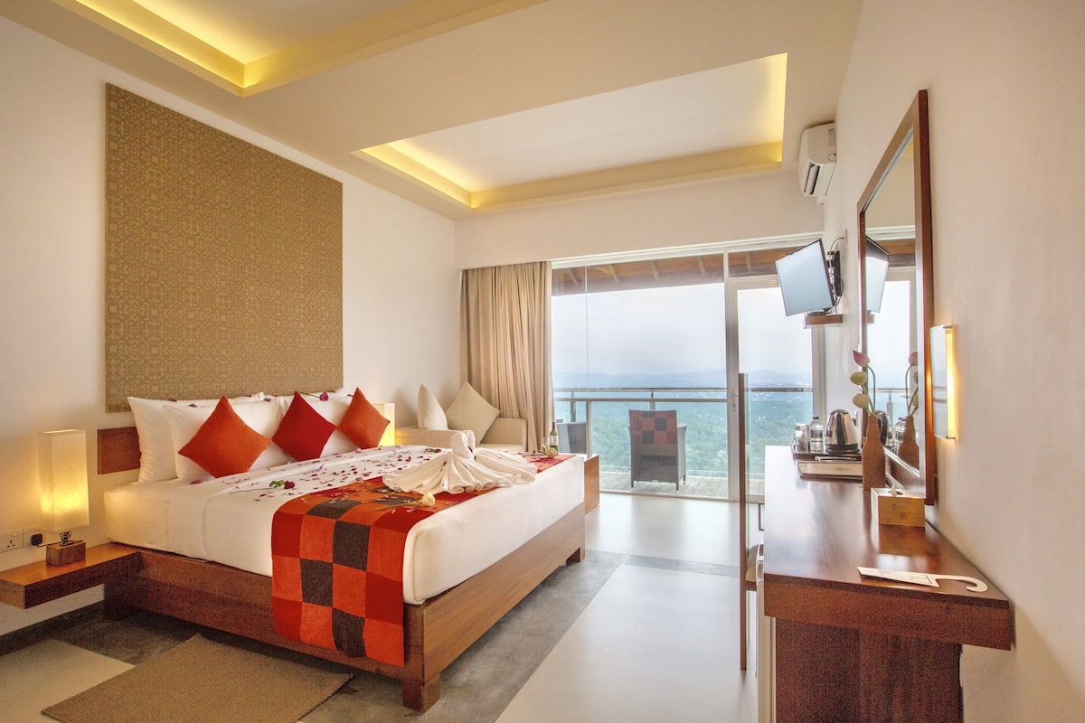 A hotel room with a large bed, a desk, and a balcony with a view.