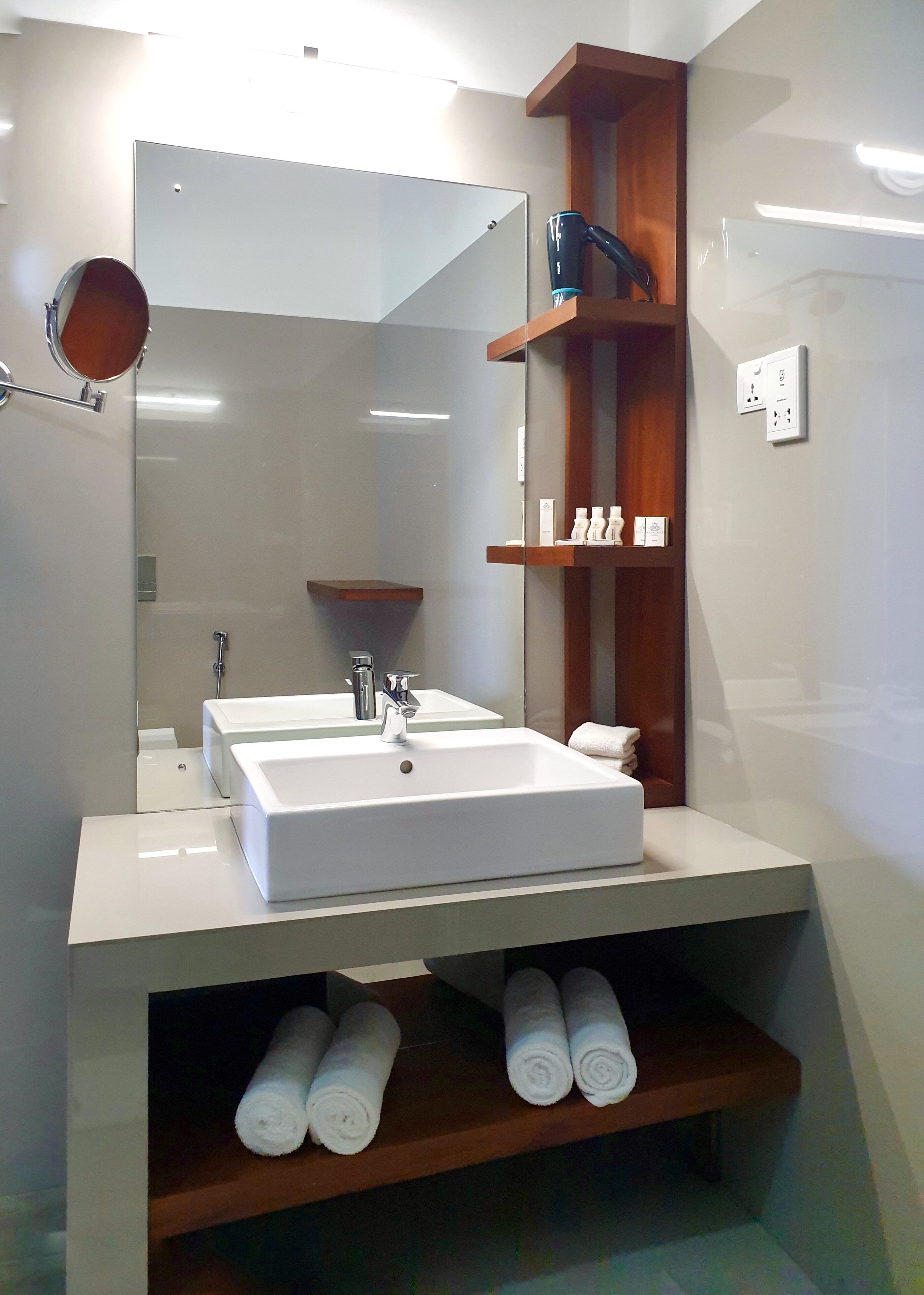A modern bathroom with a large mirror, two sinks, and a wooden shelf with towels.