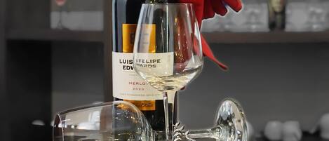 A bottle of Luis Eduardo Merlot 2020 wine with a red bow, a wine glass, and a decanter on a reflective surface.
