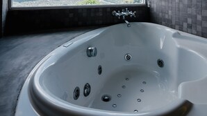 A modern bathroom with a large bathtub, a view of the sky and clouds, and a tiled wall.